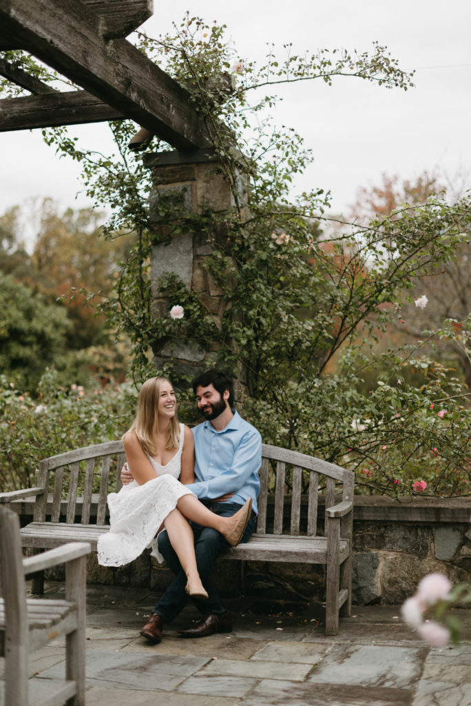 A couple laughs as they cuddle up on a bench in a rose garden. virginia wedding venue