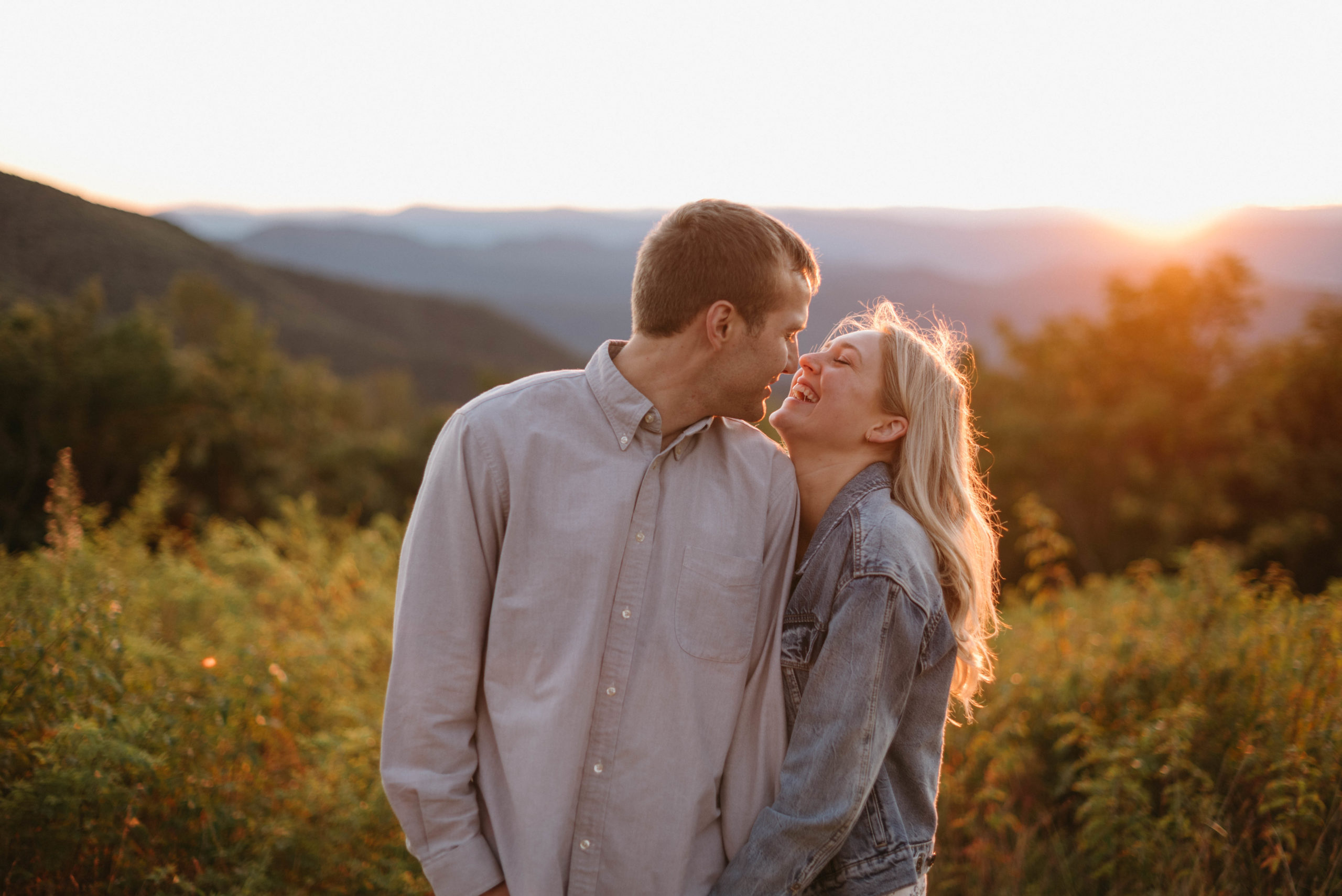 couple laughs in the mountains as the sun sets behind them