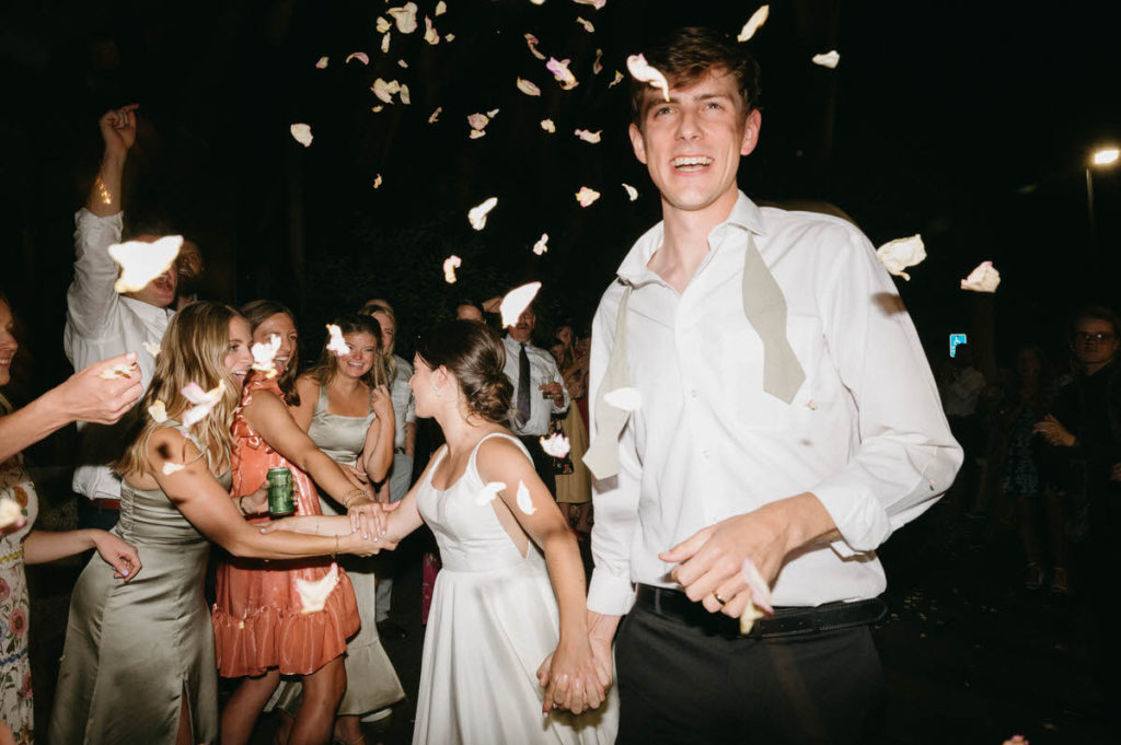 bride and groom holding hands and smiling as confetti falls 