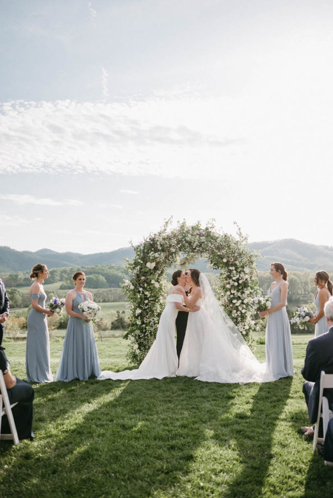 two brides during their first kiss with their wedding parties around them