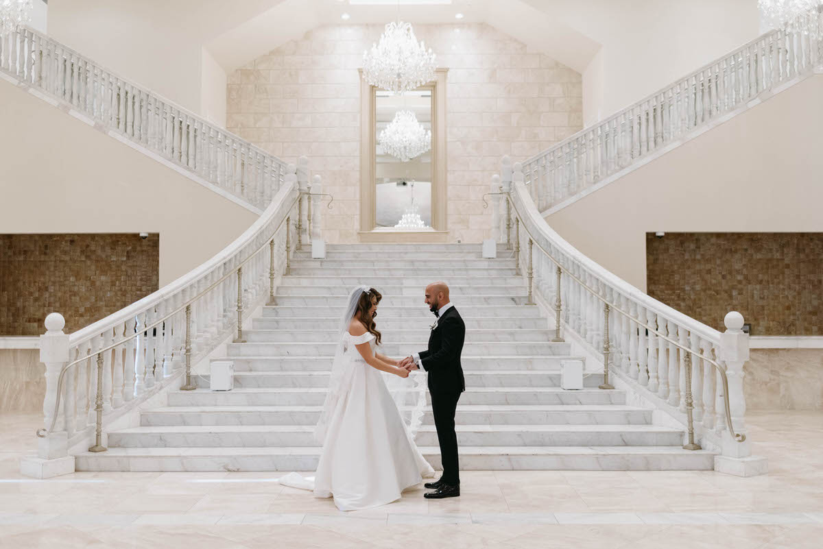 wedding couple holding hands and looking at each other at the foot of a grand staircase