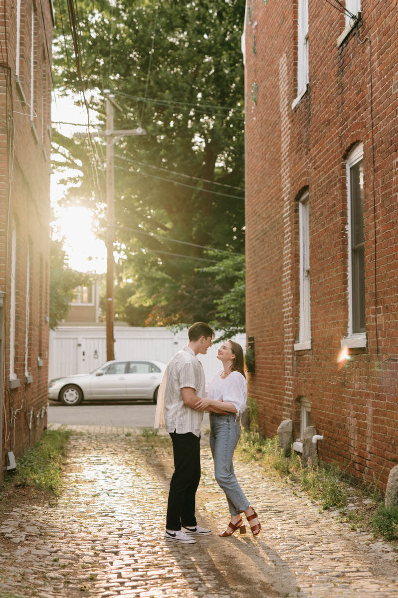 couple holding each other while in the middle of an alley between two brick buildings