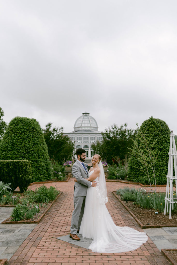 A couple laughs after getting married in front of a greenhouse in Lewis Ginter Botanical Gardens
