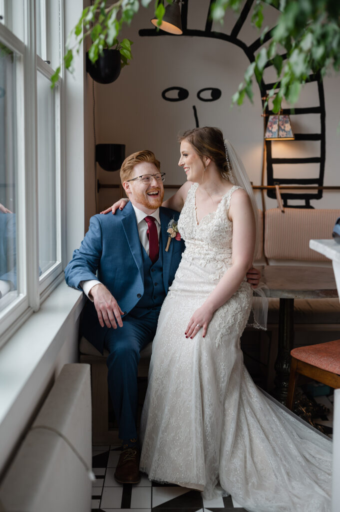a bride and groom snuggle close while laughing together looking out a window at common house in charlottesville virginia