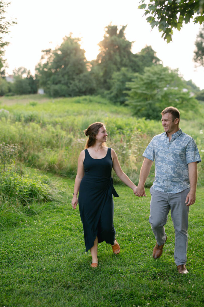 A couple holding hands and smiling at each other as they walk through a field. 