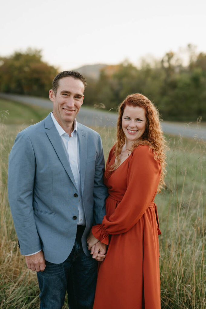 A couple holding hands and smiling in a small field. 