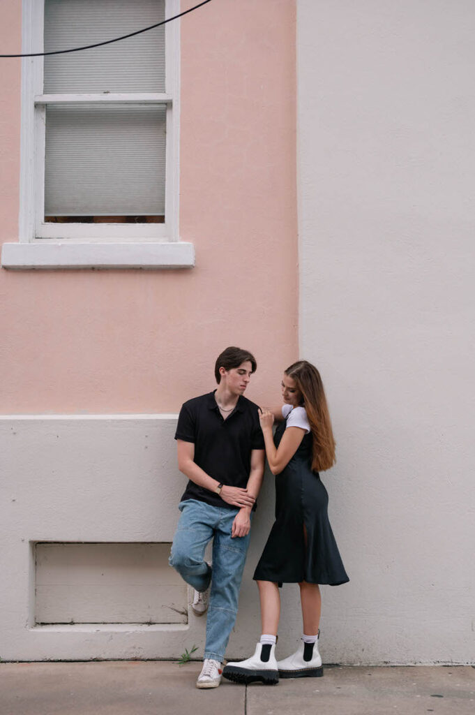 A couple leaning up against a colorful wall and looking at each other. 