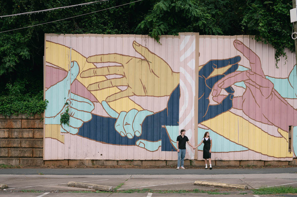 A couple holding hands and standing in front of a large mural at one of the best places to take pictures in Charlottesville VA.