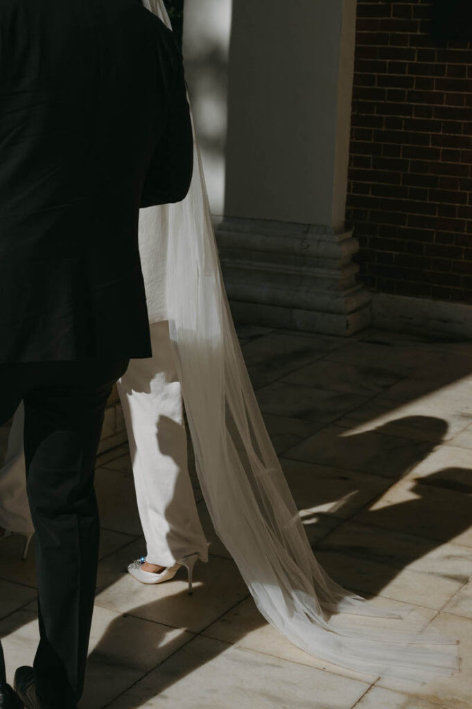 A wedding couple walking along the outside of a brick building. 