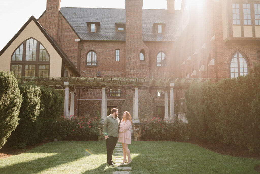 A couple standing in a small garden area with a large red brick building behind them.