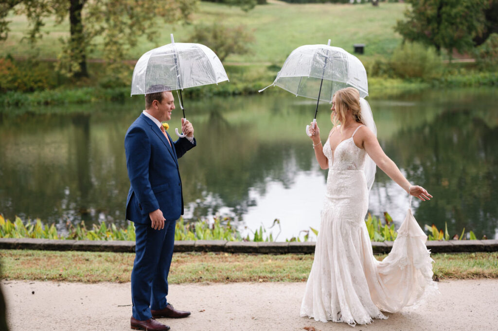 A bride and groom standing next to each other while holding clear umbrellas. 