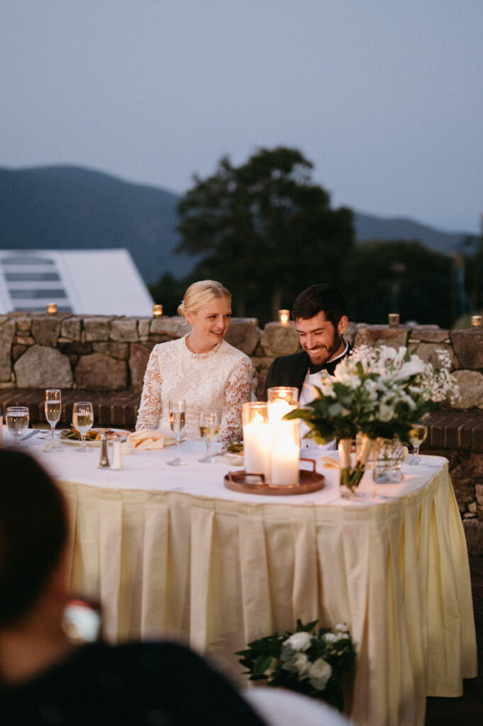 A bride and groom sitting at a table at their reception.