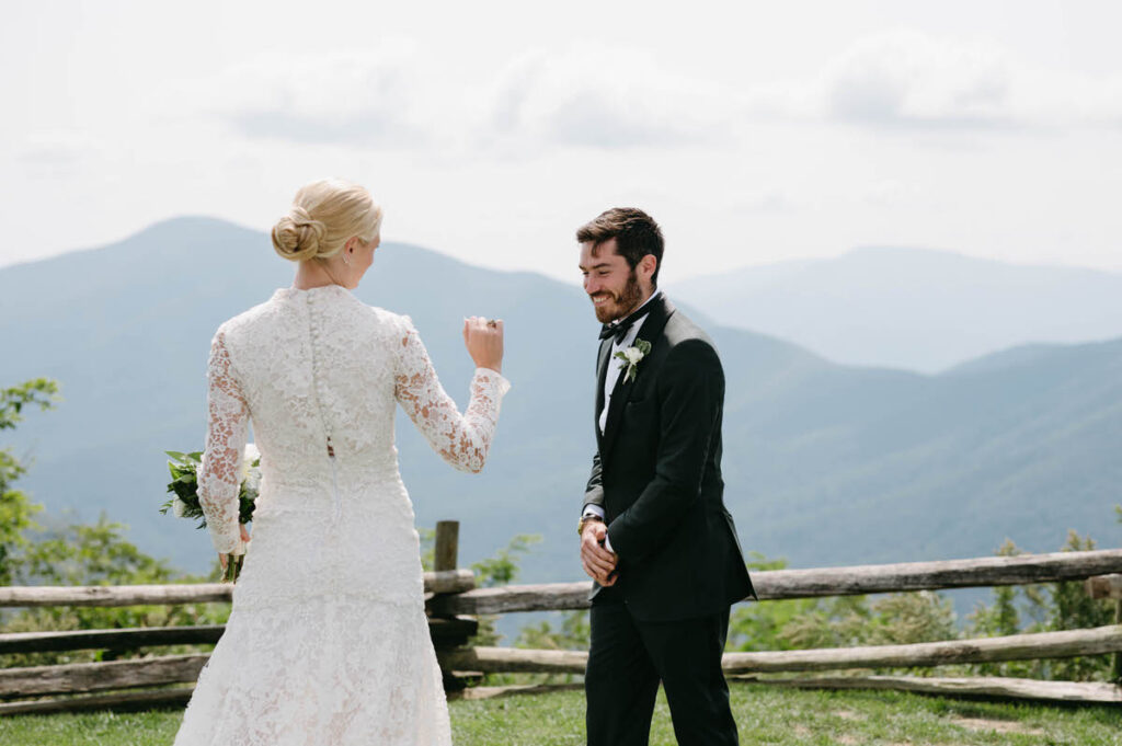 A wedding couple during their first look on an overlook with views of the mountains. 