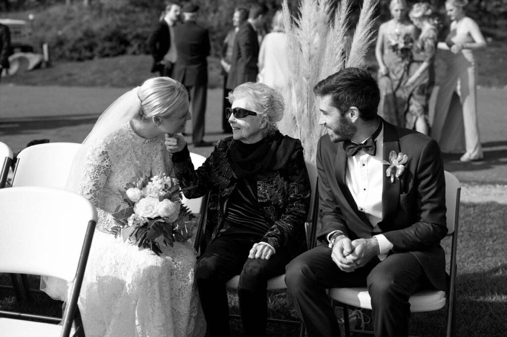 A bride and groom sitting on either side of an elderly woman. 