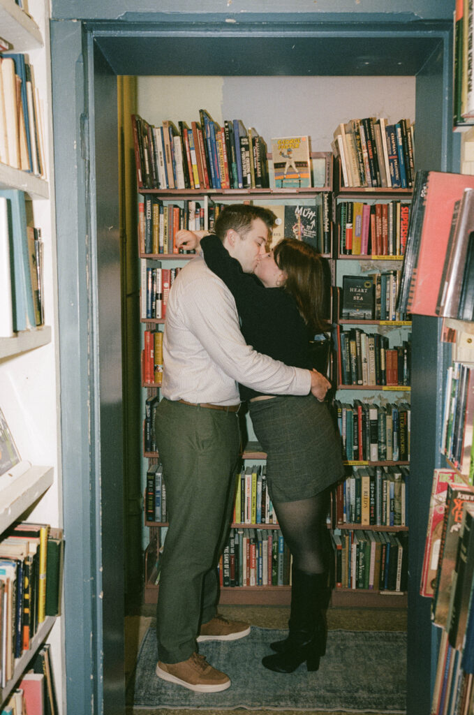 A couple sneaks a kiss in the aisle of a bookstore