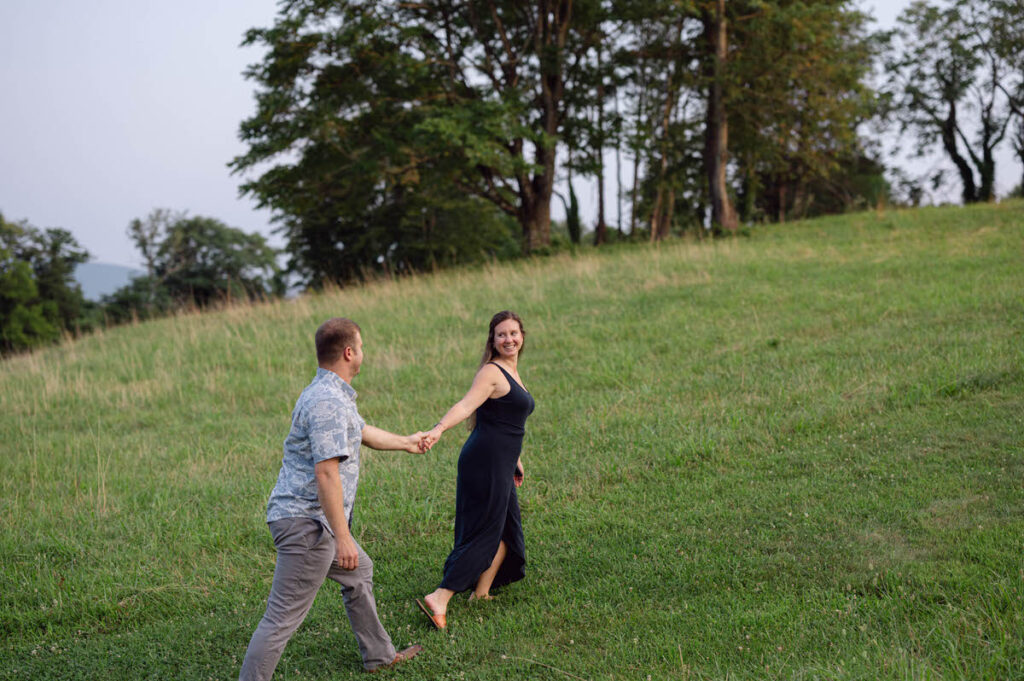 A couple with their arms outstretched holding hands and walking up the side of a grassy hill. 