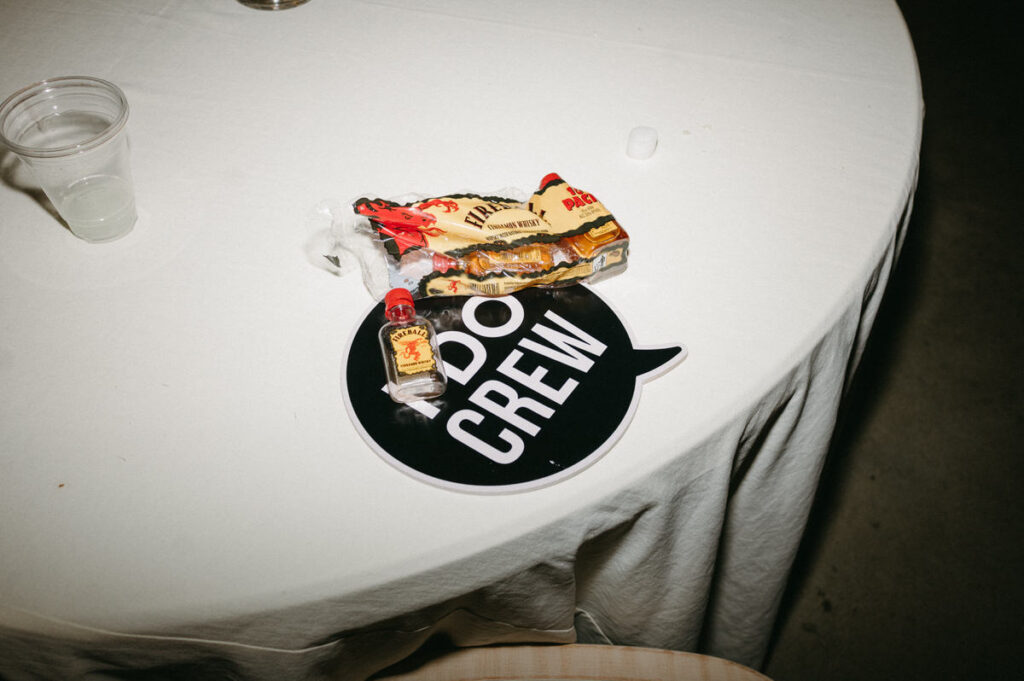 A wedding reception table with Fireball nips and a sign that reads "I do crew". 