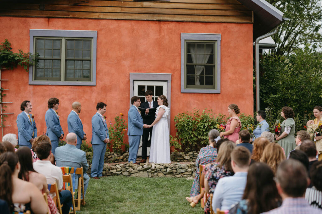 A couple standing up during their wedding ceremony with their guests watching them. 
