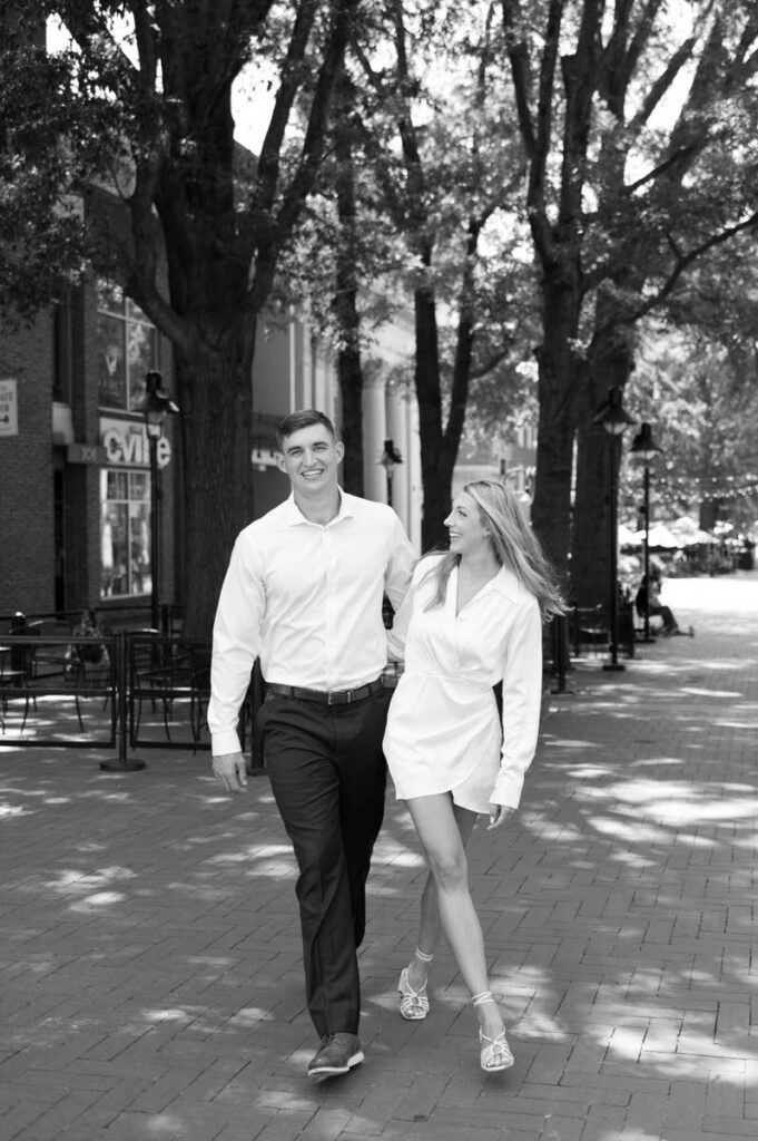 A couple walking along a brick sidewalk laughing. 
