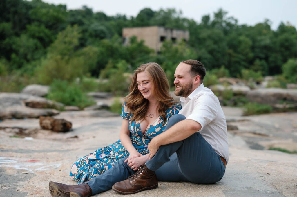 A couple sitting on a rocky areas together smiling. 
