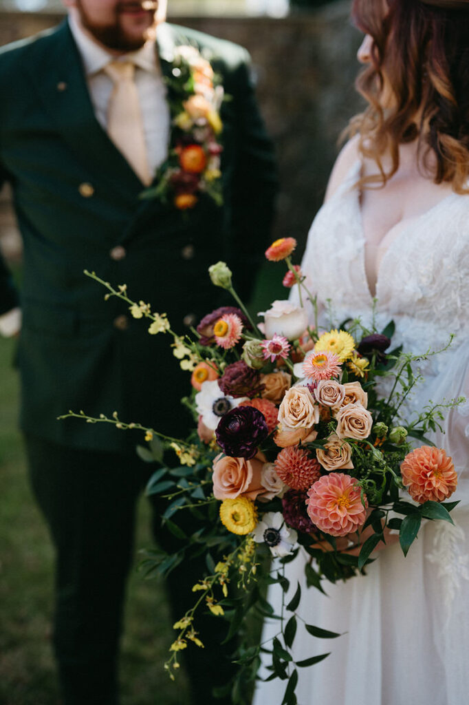 "Close-up of the bride and groom holding hands, showcasing the intricate details of the bride's bouquet and the groom's boutonniere, set against their wedding attire