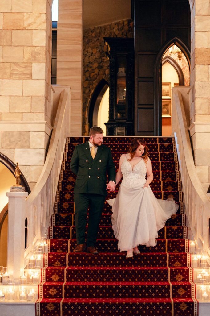 The bride and groom descend a grand staircase adorned with candles, capturing a romantic moment within the luxurious interior of Dover Hall.