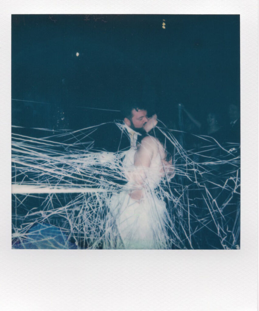 A Polaroid of a bride and groom enveloped in a whimsical cloud of streamers, creating a dreamlike atmosphere in a candid wedding moment