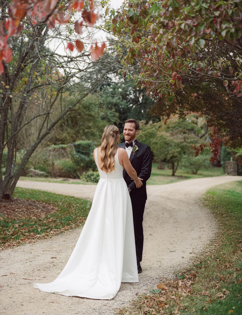 A man and woman see each other for the first time on their wedding day, the groom happily smiles at his soon-to-be wife under fall foliage 