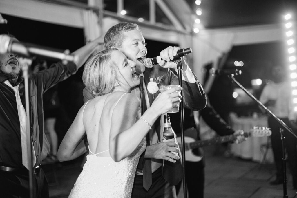A newlywed couple standing at a microphone singing with a band 
