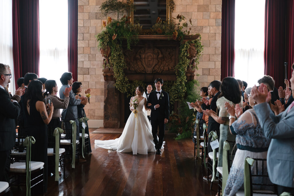 A bride and groom walk back down the aisle with big smiles after just finishing their wedding ceremony as their friends and family cheer