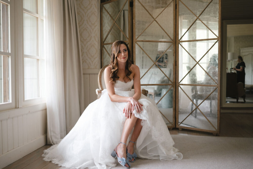 A person in a wedding dress sitting in a chair showing off their shoes. 