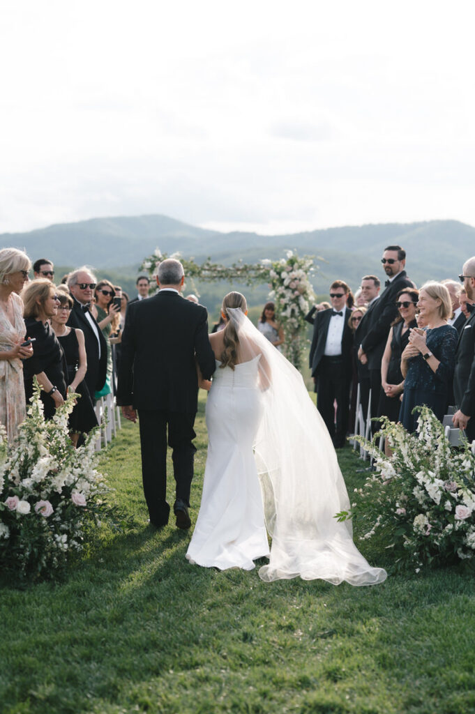 A parent walking their child down the aisle at an outdoor wedding. 