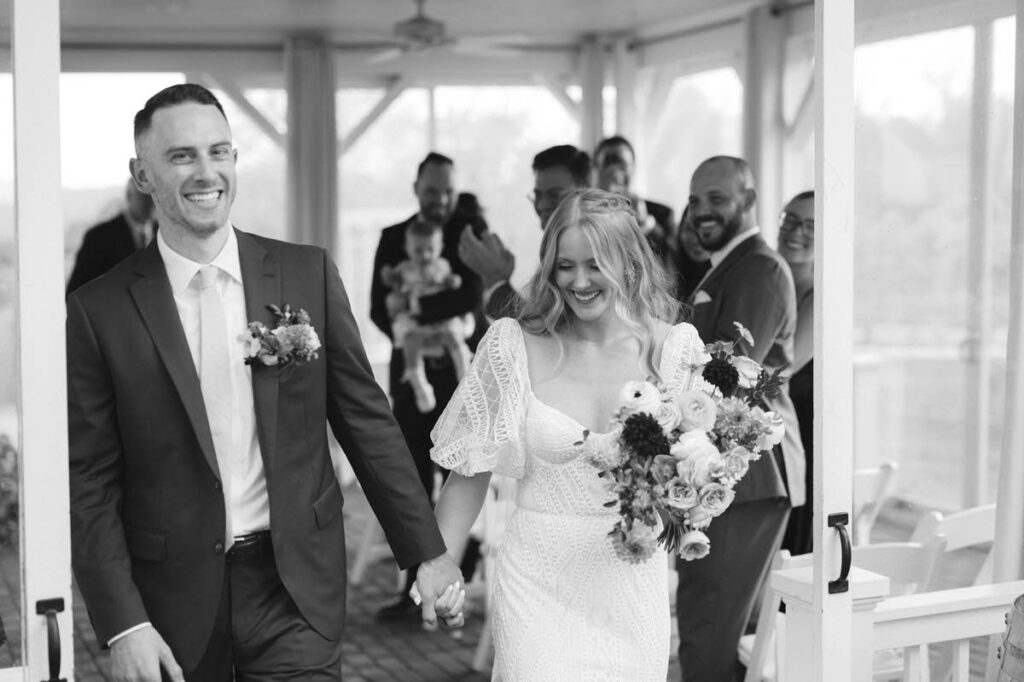 A newlywed couple holding hands and walking back up the aisle together. 