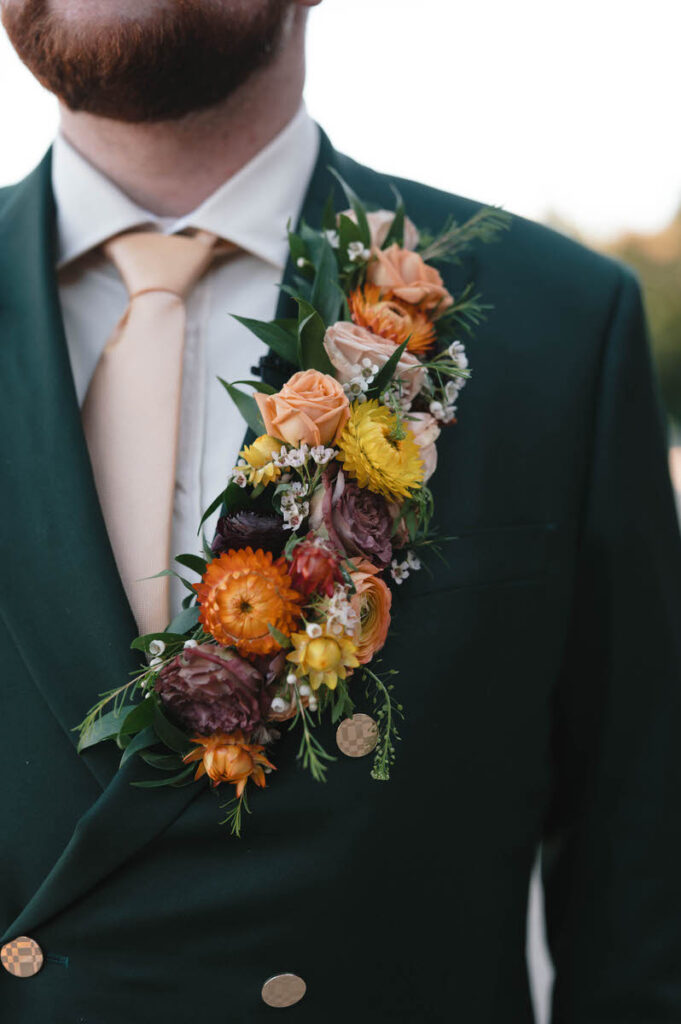 A close-up of the groom’s dark green suit jacket adorned with a detailed floral arrangement featuring roses and mixed flowers in a cascade design.