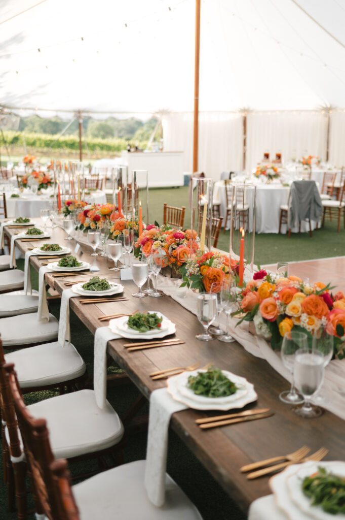 Wedding reception tables decorated with bright flower and candles under a large tent 