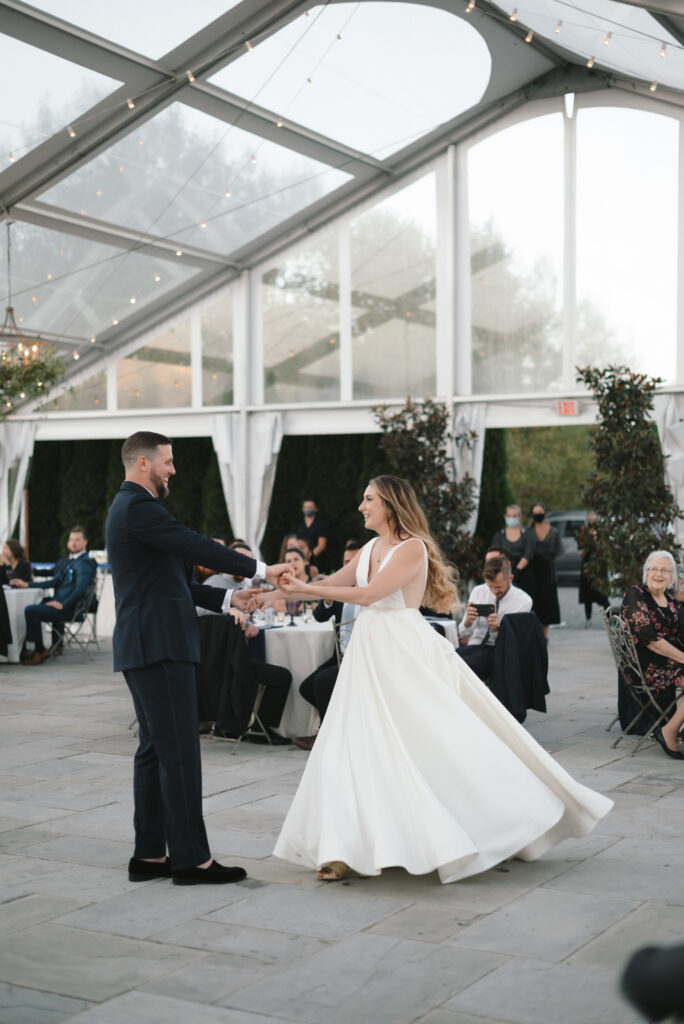 A newlywed couple during their first dance under a clear top tent 