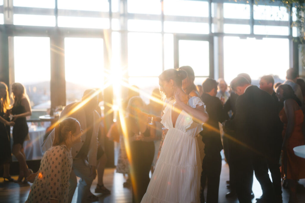 Sun shinning through the window and wedding guests dance at a reception. 