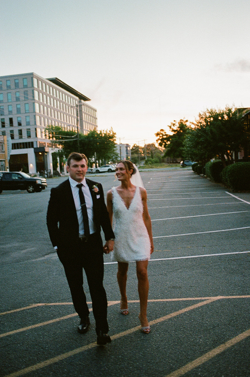 Unique wedding photos of a couple holding hands and walking through a parking lot at dusk