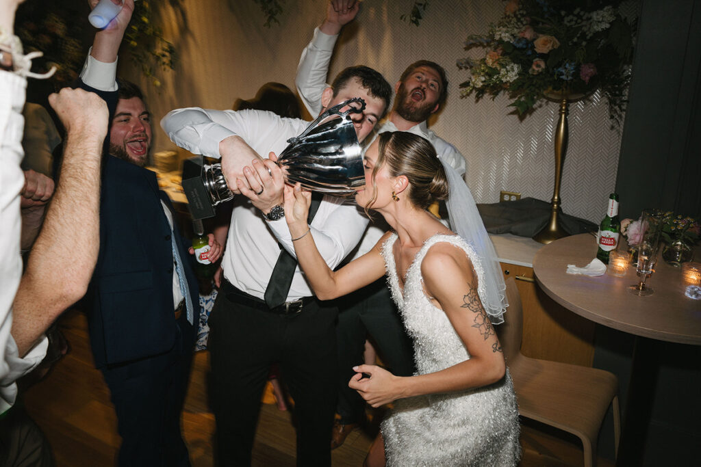 A person in a wedding dress drinking out of a large trophy 