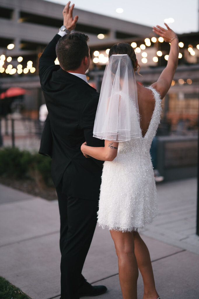 A newlywed couple waving back at their guests 