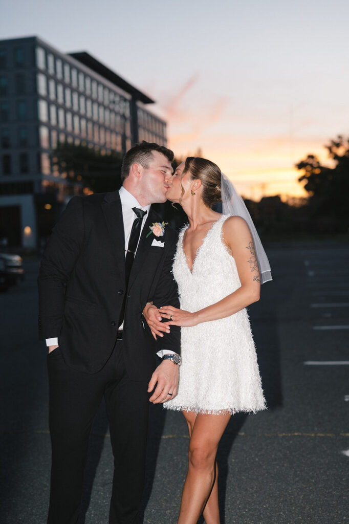 A newlywed couple kissing in a parking lot 