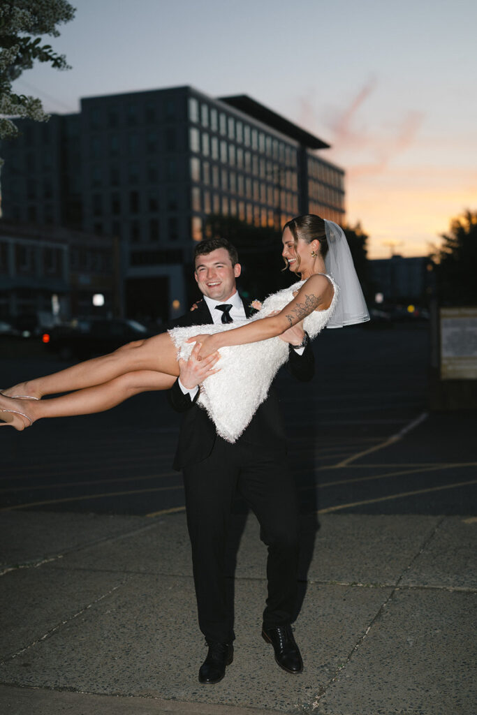 A newlywed lifting up their partner as they both smile 