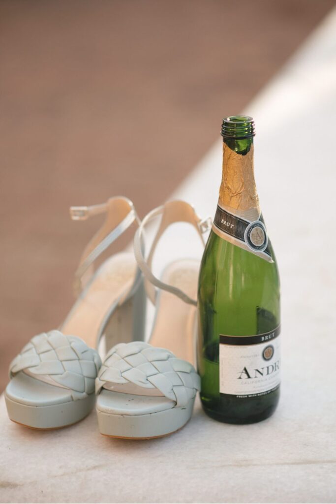  A pair of light blue woven sandals next to a bottle of André Brut champagne on a marble surface, capturing a celebratory moment.