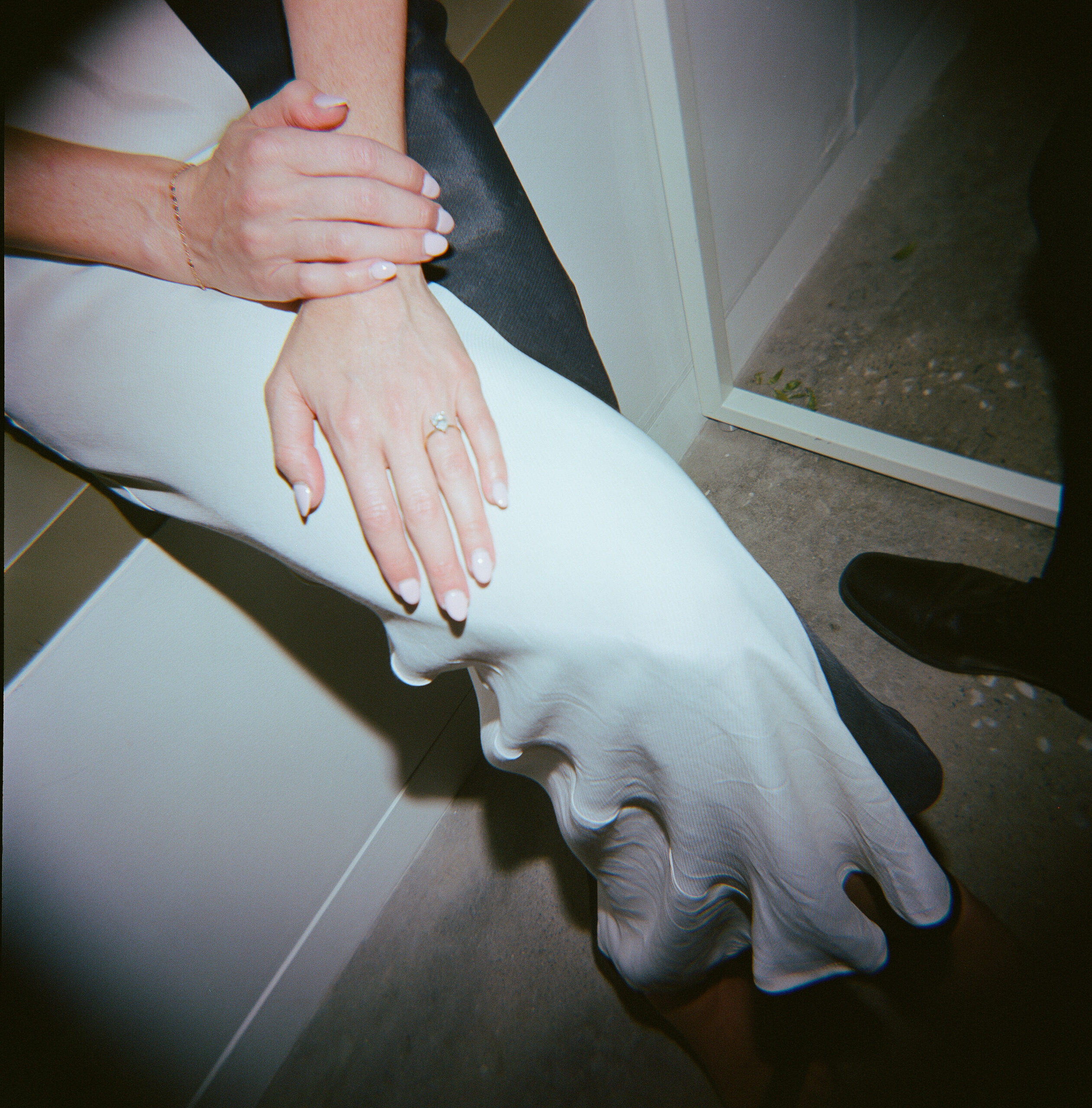 A woman in a black and white dress sitting down you can see her hands with her fingernails painted white and her engagment ring 