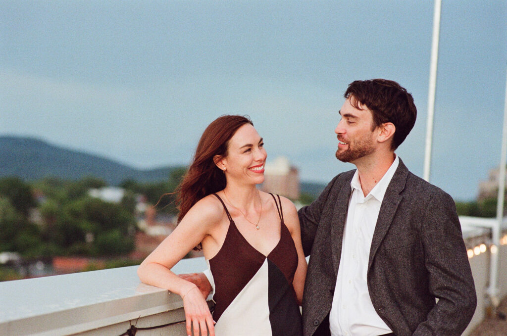 a couple with a woman in a black and white dress and a man in a button up and blazer looking at each other and laughing 