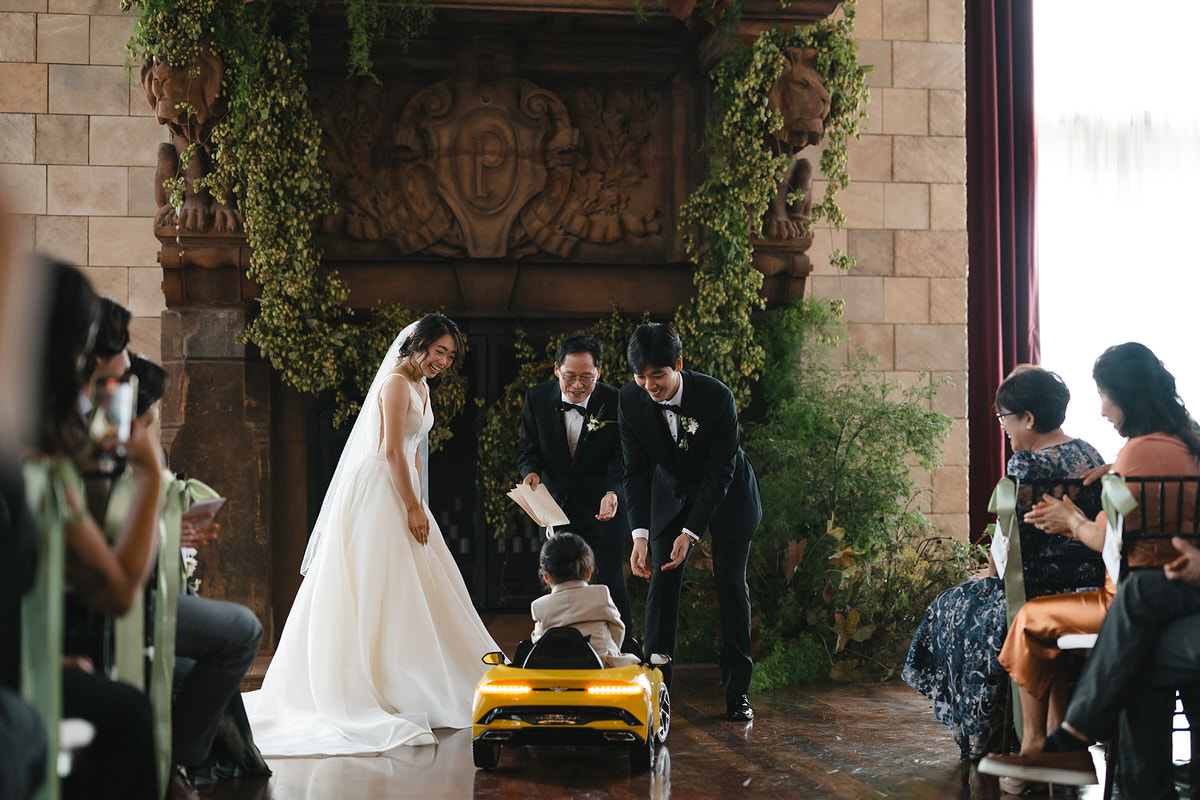 A one of a kind wedding photo with a ring bearer driving down the aisle in a mini car to deliver the rings to a couple