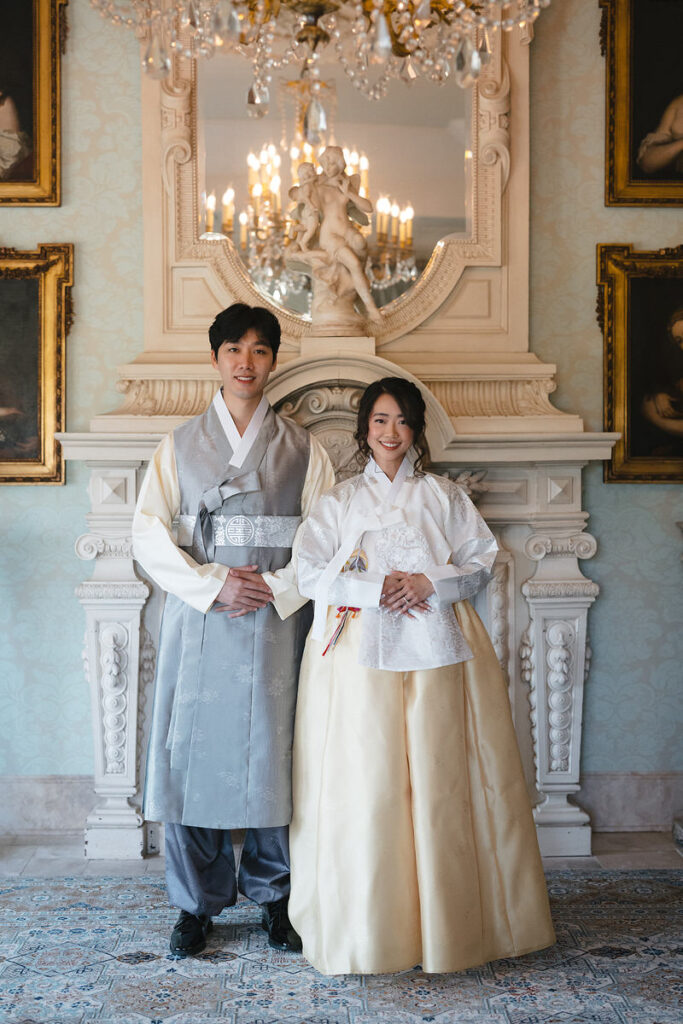 A couple in traditional Korean outfits standing together and smiling. 