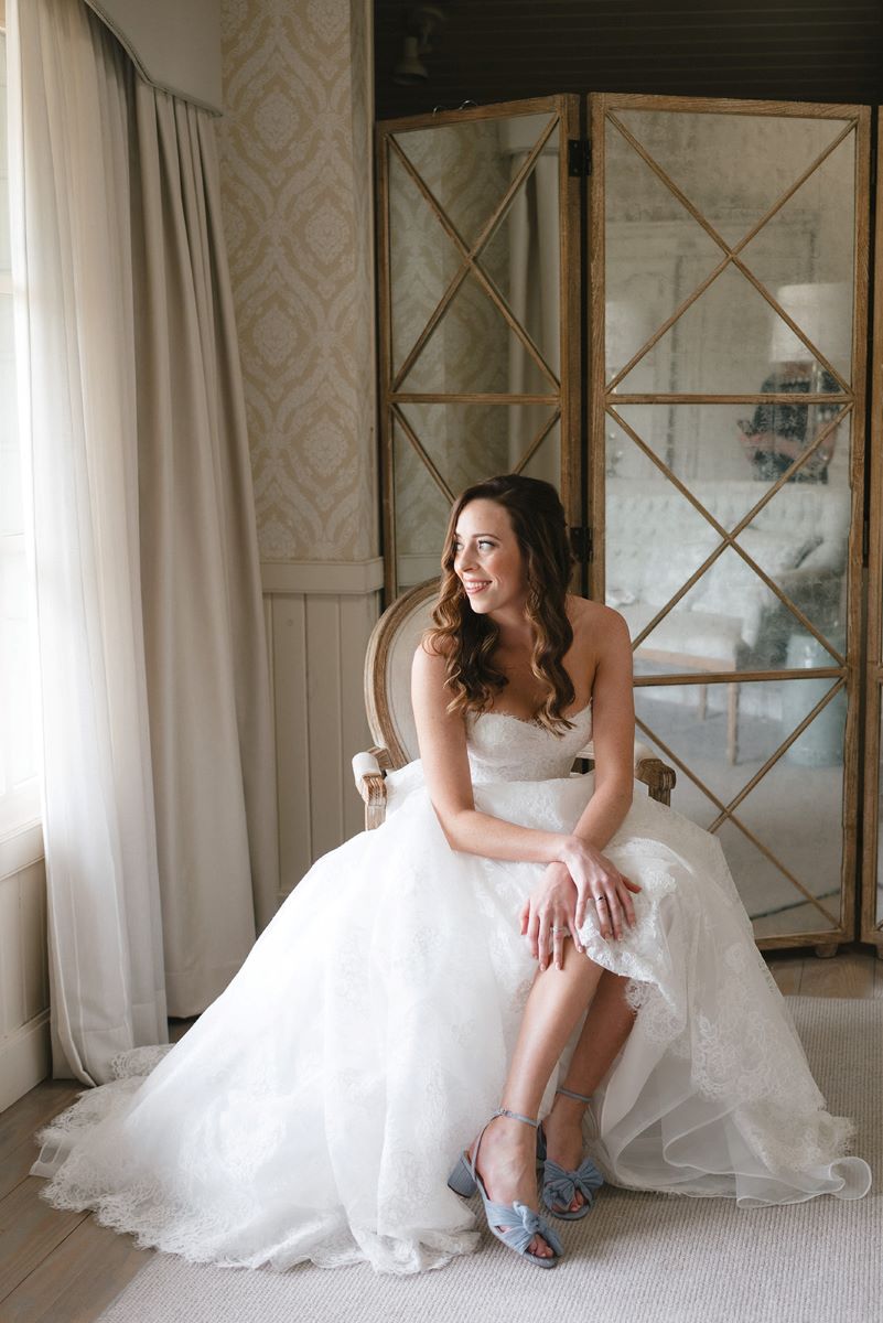 woman in a wedding dress with blue heels sitting on a chair and looking out the window 