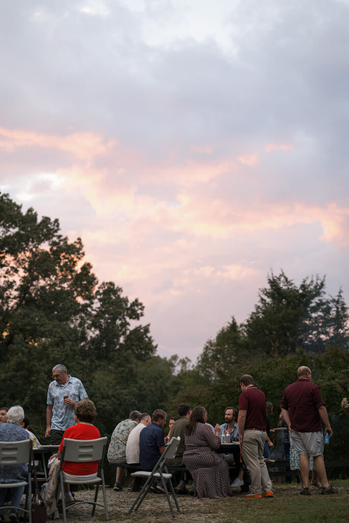 Guests sit outdoors under a colorful evening sky with hues of pink and purple during cocktail hour.