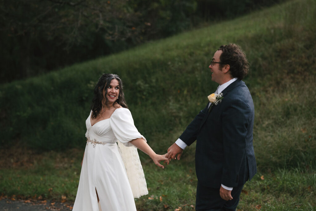 The couple walks hand in hand in a forested area.